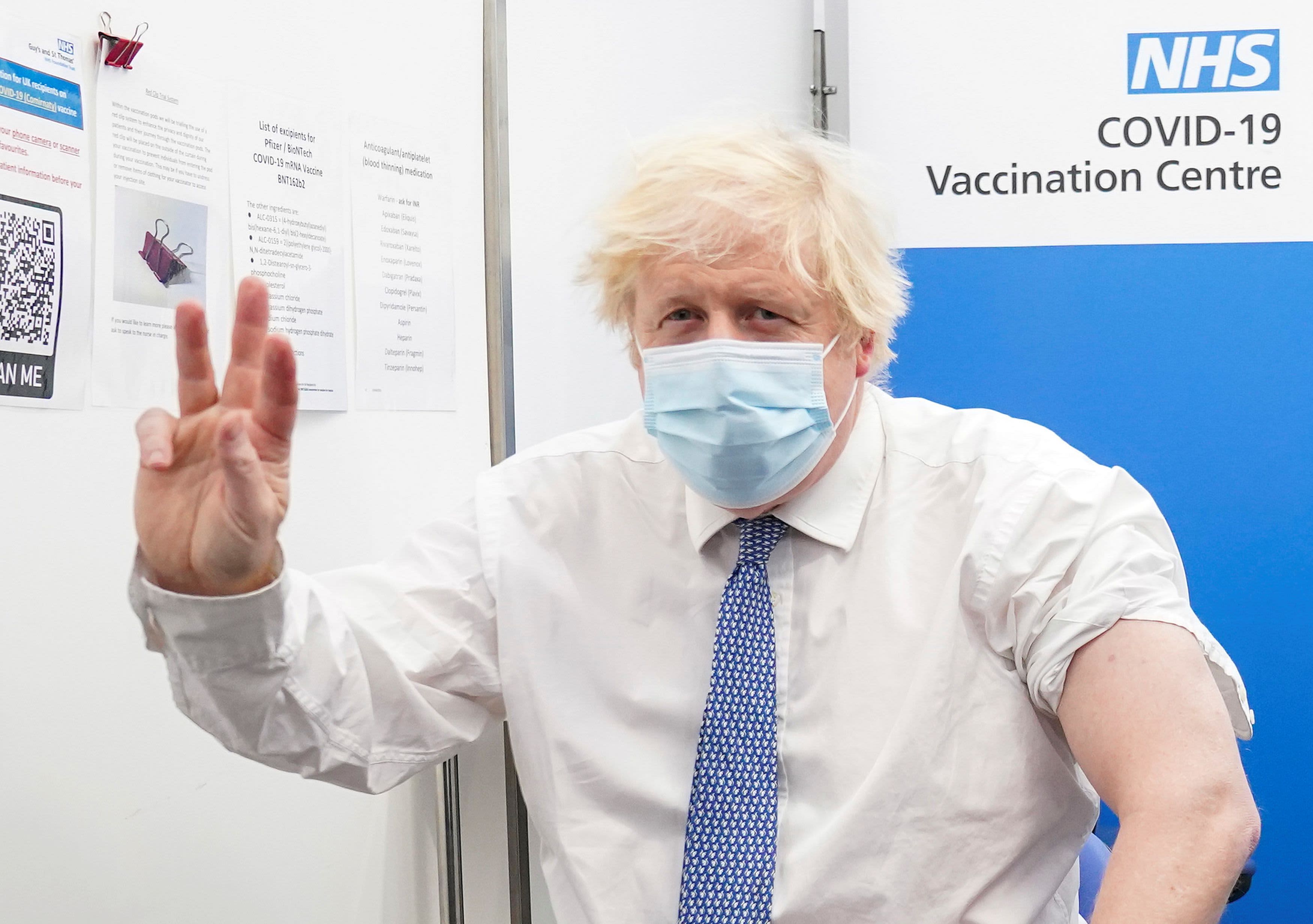 Boris Johnson in a face mask giving a victory sign at an NHS COVID-19 vaccination centre.