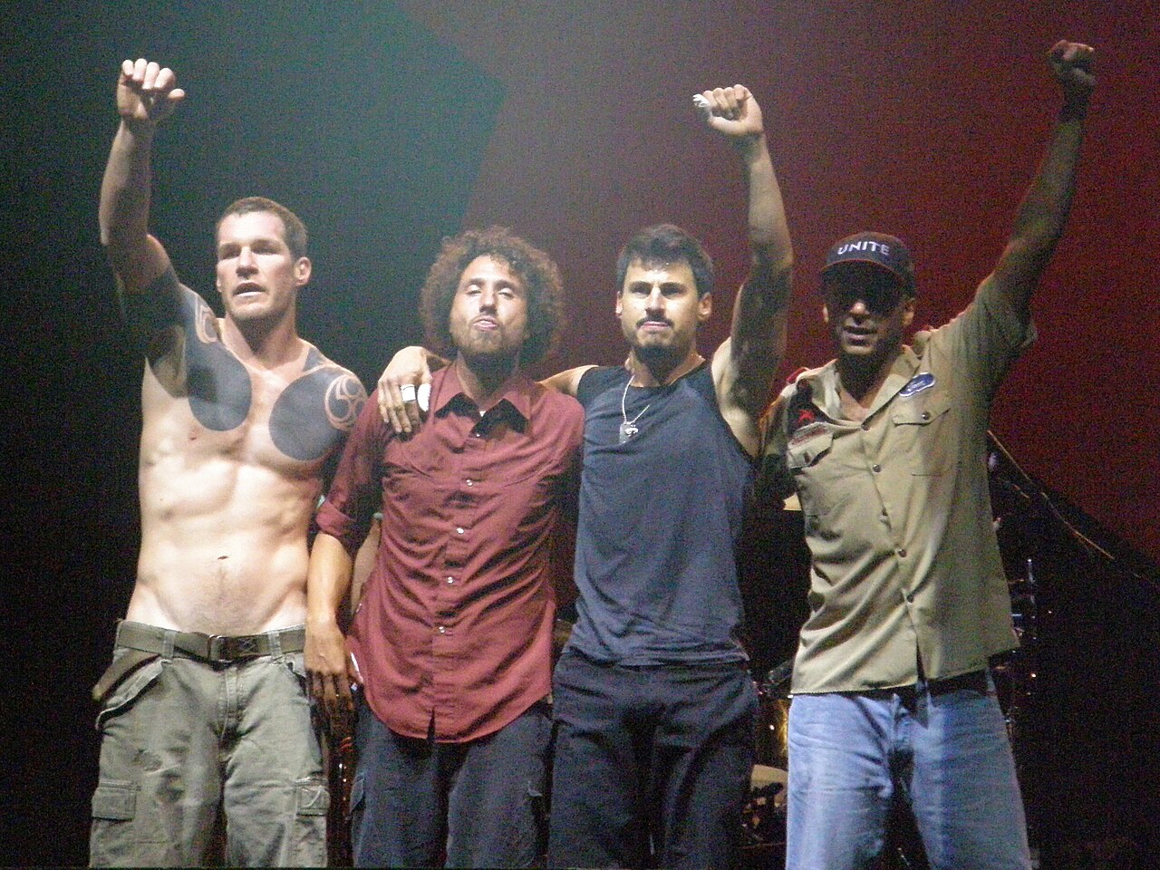 The four members of Rage Against the Machine standing on stage with fists raised.