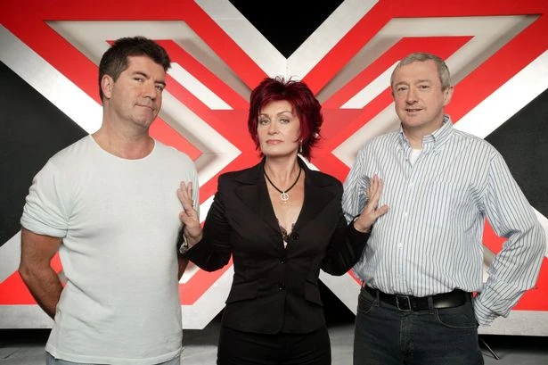 The X Factor judges Simon Cowell, Sharon Osbourne and Louis Walsh in front of the show’s red X logo.