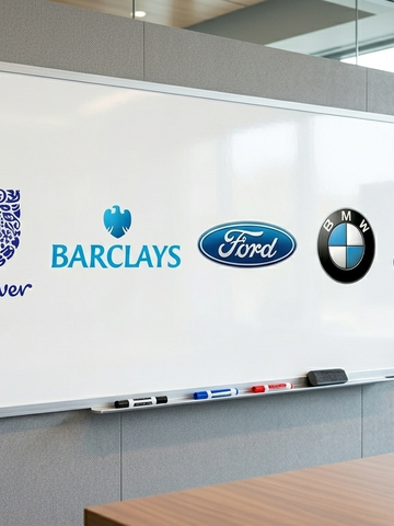 A meeting-room whiteboard displaying the Unilever, Barclays, Ford, BMW and Confused.com logos, with a hand gesturing towards it.
