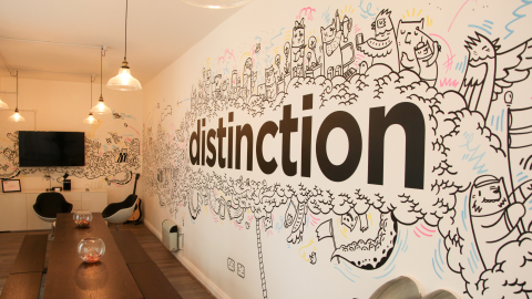 An office meeting room wall covered in a hand-drawn doodle mural with the word “distinction” in bold black lowercase across the centre.