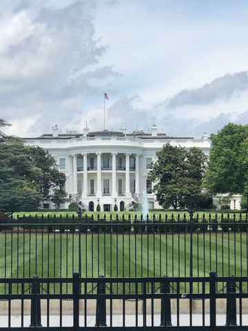 The White House seen across its lawn and security railings, with a red “Restricted Area – Do Not Enter” sign on the fence.